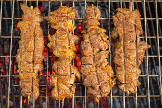 Skewers of meat cooking on a grill with visible flames.